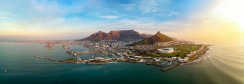 Atemberaubendes Panorama von Kapstadt bei Sonnenaufgang, mit Blick auf den Tafelberg, den Lion’s Head und das glitzernde Meer. Die Waterfront, das markante Stadion und der geschäftige Hafen zeigen die pulsierende Metropole Südafrikas. Ein perfektes Reiseziel für Luxusreisen, Abenteuer und unvergessliche Erlebnisse an der Südspitze Afrikas
