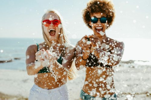 Excited,Young,Women,Friends,Bursting,A,Water,Balloon,And,Smiling